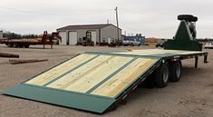 a flatbed trailer parked in a parking lot next to other trucks and equipment on the ground