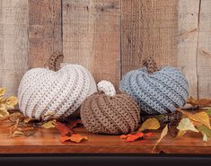 three knitted pumpkins sitting on top of a wooden table next to autumn leaves