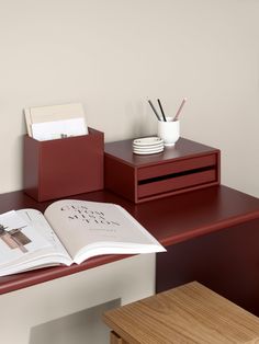 an open book sitting on top of a wooden desk next to a cup and pen holder