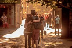 two people hugging each other on the sidewalk in front of a group of people walking down the street