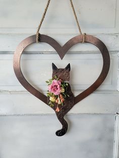 a metal heart with a cat and flowers hanging from it's side on a door