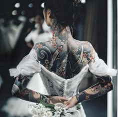 the back of a woman's body covered in tattoos and holding a bouquet of flowers