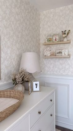 a baby's room with white furniture and floral wallpaper