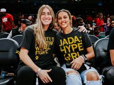 two women sitting next to each other in front of a crowd at a basketball game