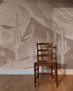 a wooden chair sitting in front of a wall with a cactus mural on it's side