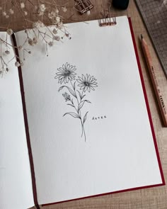 an open notebook with flowers drawn on it next to a pencil and some other items