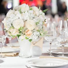 a white vase filled with flowers sitting on top of a table next to wine glasses