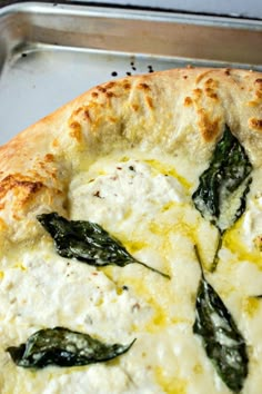 a close up of a pizza with cheese and spinach leaves on it, in a metal pan