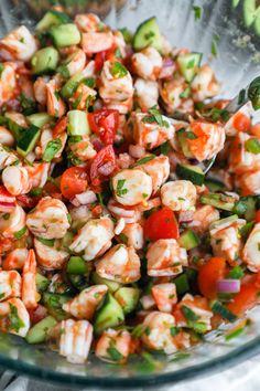 shrimp salad with tomatoes, cucumbers and parsley in a glass bowl on a table