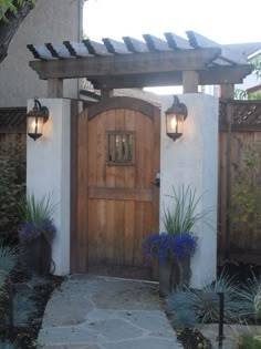 an entrance to a home with two lights on the side and blue flowers in front