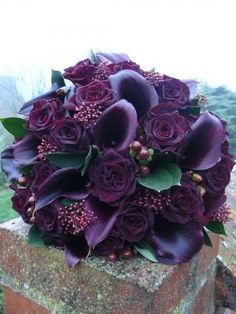 a bridal bouquet with purple flowers on top of a stone wall in the countryside