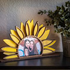 a wooden sunflower frame with two girls in the center on a shelf next to a potted plant