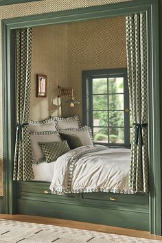 a bed sitting under a window next to a green frame with curtains and pillows on it