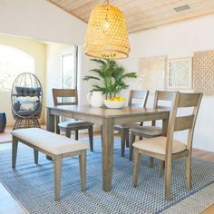 a dining room table with chairs and a bench in front of an area rug that has a potted plant on it