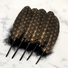 five black and gold fan shaped hair combs on a white marble counter top with feathers