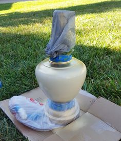 a large white vase sitting on top of a cardboard box in the middle of grass