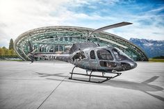 a helicopter is parked in front of a large glass building with mountains in the background