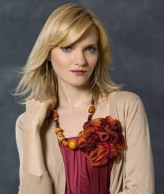 a woman with blonde hair wearing a brown cardigan and beaded necklace is posing for the camera