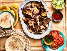 a platter with chicken, tomatoes, cucumbers and pita bread