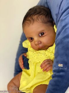 a baby in a yellow dress sitting on a blue pillow