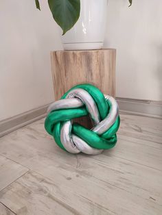 a green and white knot sitting on top of a hard wood floor next to a potted plant