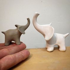 two small elephants are standing next to each other on a wooden table with a person's hand