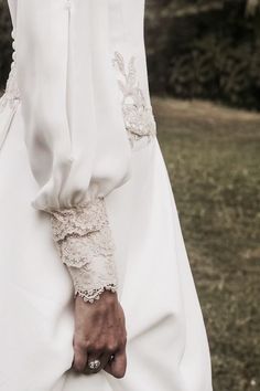 a woman's white dress with lace on the sleeves and cuffs, in front of a grassy field