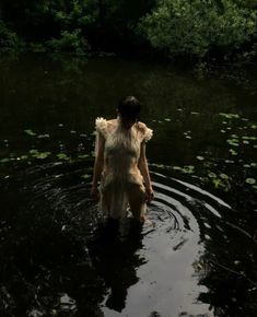 a woman is wading in the water with her back turned to the camera and looking down