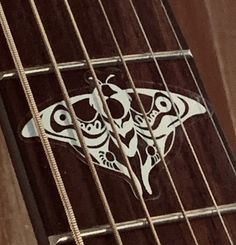 a close up of an acoustic guitar's neck and fret with a moth sticker on it