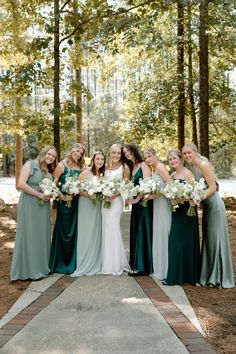 a group of women standing next to each other holding bouquets in front of trees