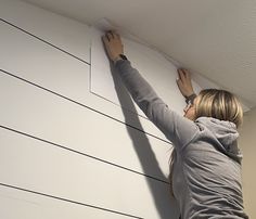 a woman is painting the wall with white paint and she has her hands on the board