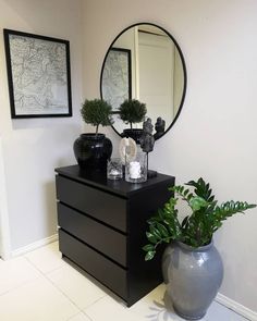 a black dresser with two vases on it and a round mirror above the drawers