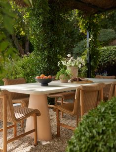 an outdoor dining table with chairs and fruit bowl on it in the middle of a garden