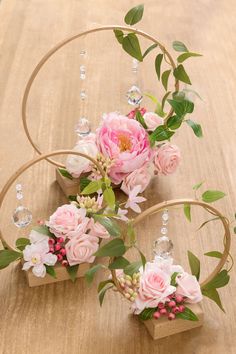 pink flowers are arranged in wooden hoop holders on a table with crystal beads and greenery