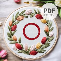 an embroidery pattern with the letter o surrounded by flowers and leaves on a wooden surface