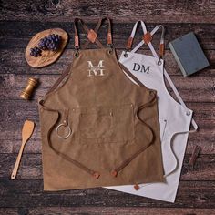 three personalized aprons are laid out on a wooden table with utensils