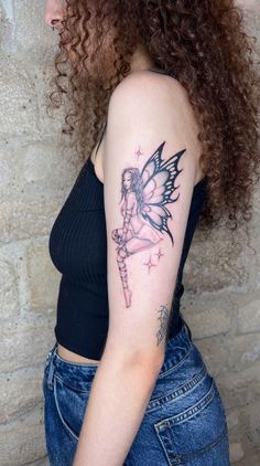 a woman with a fairy tattoo on her arm and shoulder, standing in front of a brick wall