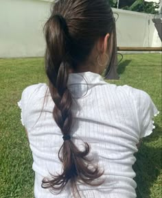 a woman sitting in the grass with her back to the camera, wearing a white shirt