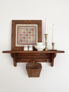 a wooden shelf with some candles on it and a basket hanging from the wall next to it