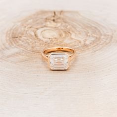 a gold ring with an emerald cut diamond in the center on top of a tree stump