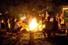 a group of people sitting around a fire pit in the middle of a park at night