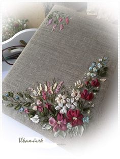 an embroidered book with flowers and leaves on the cover is sitting on a table next to some glasses