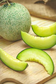 a melon and two pieces of cucumber on a cutting board next to each other