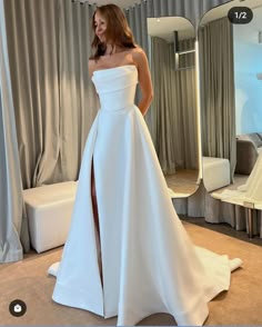 a woman standing in front of a mirror wearing a white wedding dress with high slit