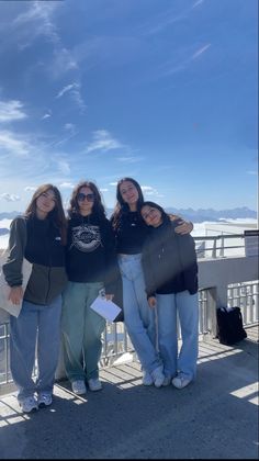 three girls are standing on a bridge with their arms around each other