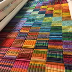 a colorful quilt is laying on the floor next to a crochet hook and yarn roller