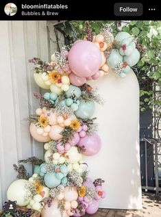 a bunch of balloons hanging from the side of a wall next to flowers and plants