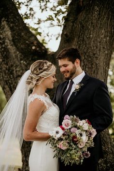 a bride and groom standing in front of a tree