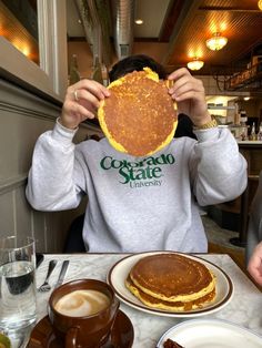 a person sitting at a table holding up a stack of pancakes