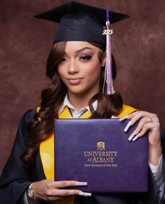 a woman wearing a graduation cap and gown holding a purple book with the university of albany written on it